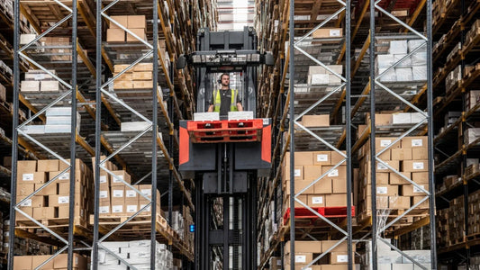 A warehouse worker stands in one of Hachette's bespoke book order picking machines which is half-raised between rows of large pallet racking