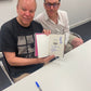 Reece Shearsmith and Steve Pemberton holding their signed book. A blue marker lies on the desk in front of them which they have used for this signed Limited Edition Book