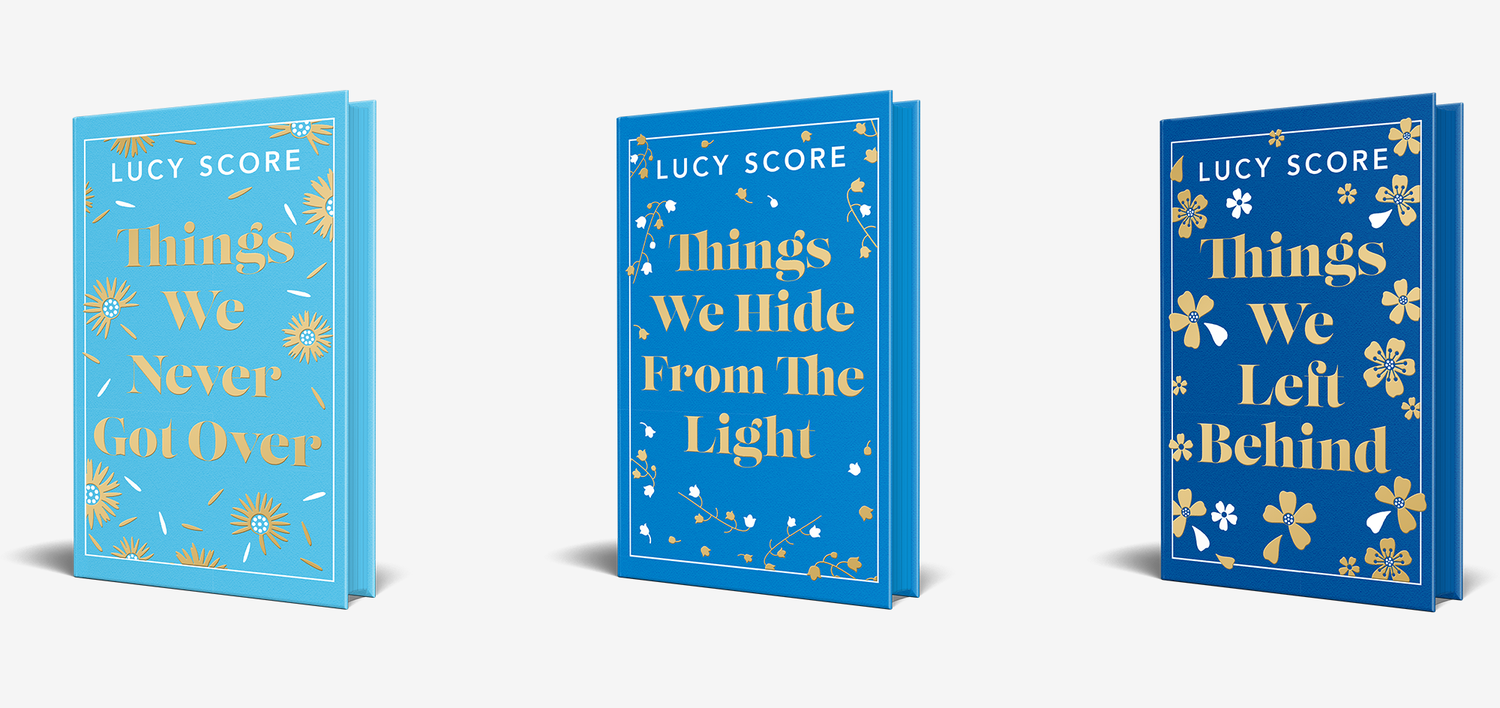 Three books by Lucy Score stand in a line with special blue covers decorated with golden flowers.